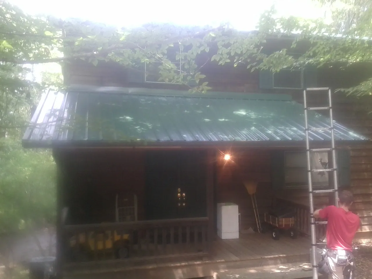 Worker on a ladder at the green porch roof of a wooded cabin in Melbourne